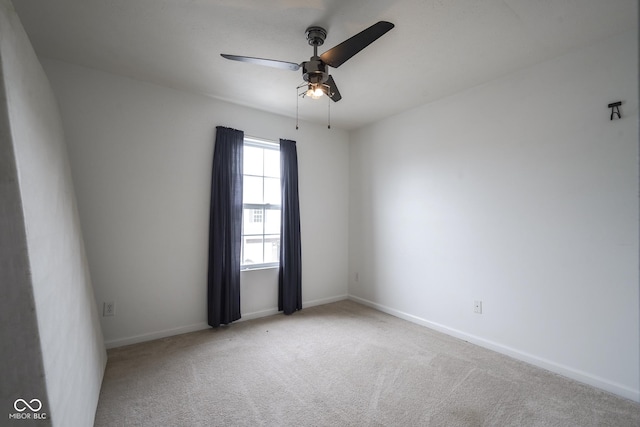 carpeted spare room featuring baseboards and a ceiling fan