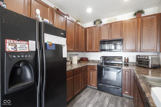 kitchen featuring light wood-style flooring, a toaster, brown cabinets, black appliances, and dark countertops