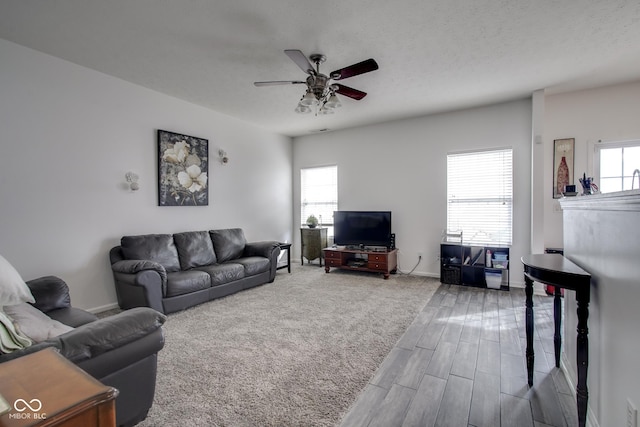 living room with ceiling fan, a textured ceiling, baseboards, and wood finished floors