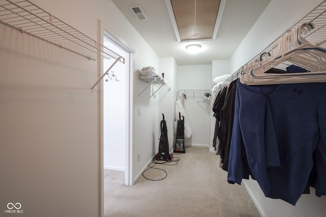 walk in closet with light colored carpet, visible vents, and attic access