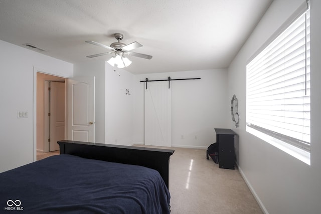 bedroom with ceiling fan, a textured ceiling, a barn door, visible vents, and baseboards