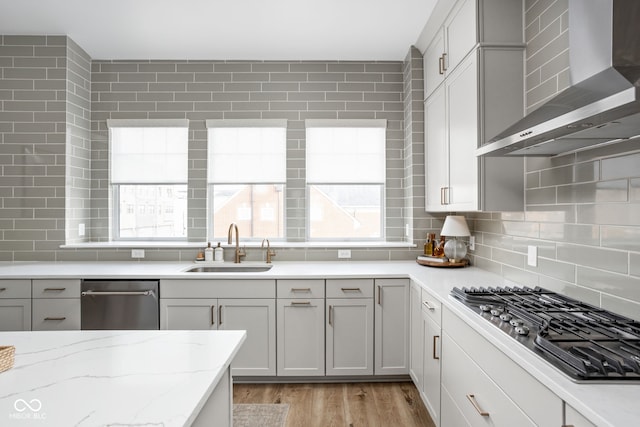 kitchen featuring light wood-style flooring, a sink, wall chimney range hood, backsplash, and stainless steel gas stovetop