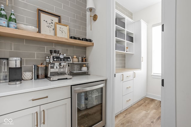 bar featuring beverage cooler, light wood finished floors, and decorative backsplash