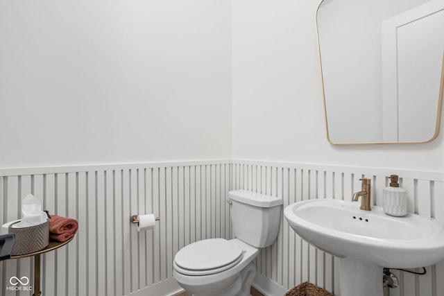 bathroom featuring a wainscoted wall, a sink, and toilet