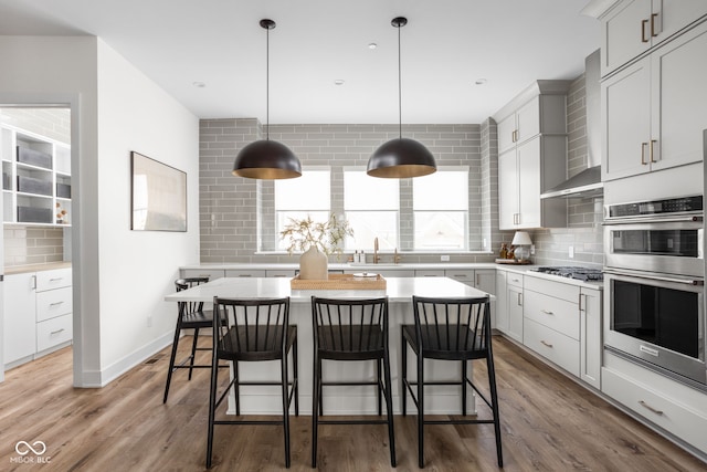 kitchen with stainless steel appliances, backsplash, wall chimney range hood, and wood finished floors