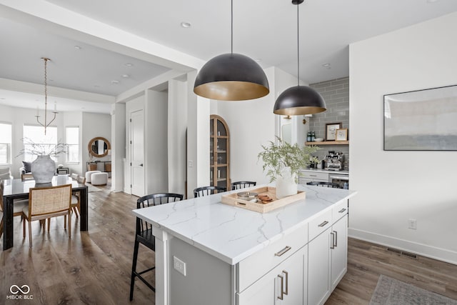 kitchen with dark wood-type flooring, a kitchen island, visible vents, a kitchen breakfast bar, and tasteful backsplash