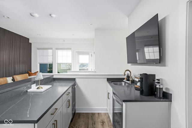 kitchen featuring dark wood-type flooring, dark countertops, a sink, and a peninsula