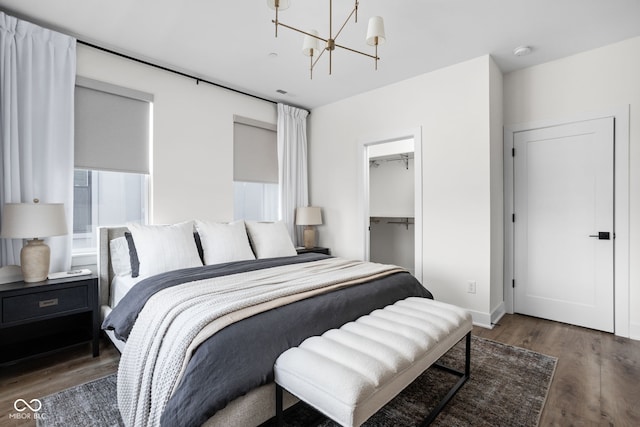 bedroom with a spacious closet, wood finished floors, and a notable chandelier