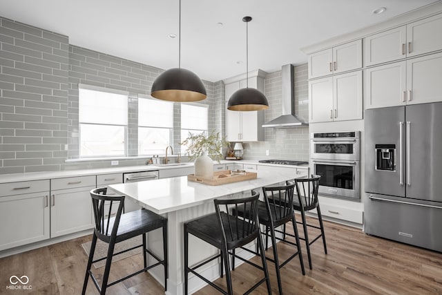 kitchen with wall chimney range hood, tasteful backsplash, appliances with stainless steel finishes, and wood finished floors