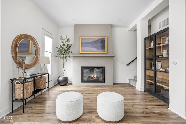 living area featuring a glass covered fireplace, stairway, wood finished floors, and visible vents