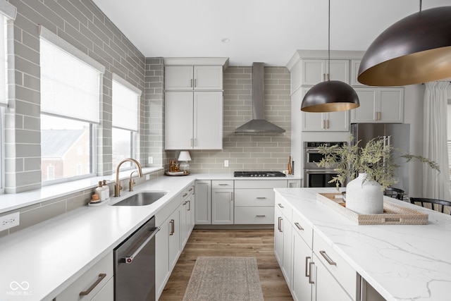 kitchen with tasteful backsplash, light wood-style floors, appliances with stainless steel finishes, wall chimney range hood, and a sink