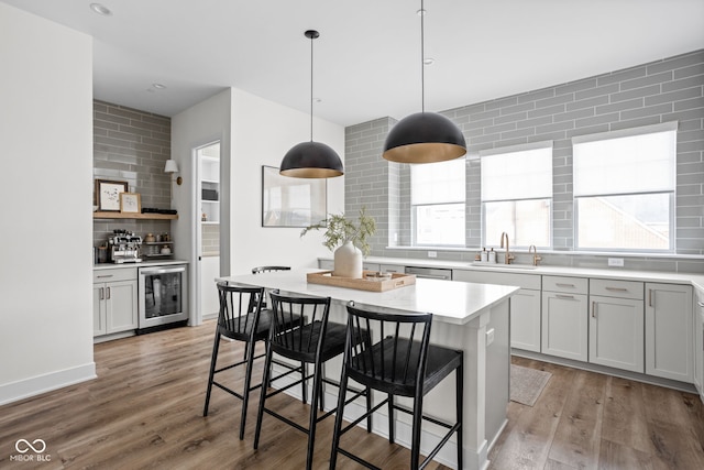 kitchen with light countertops, backsplash, a sink, wood finished floors, and beverage cooler