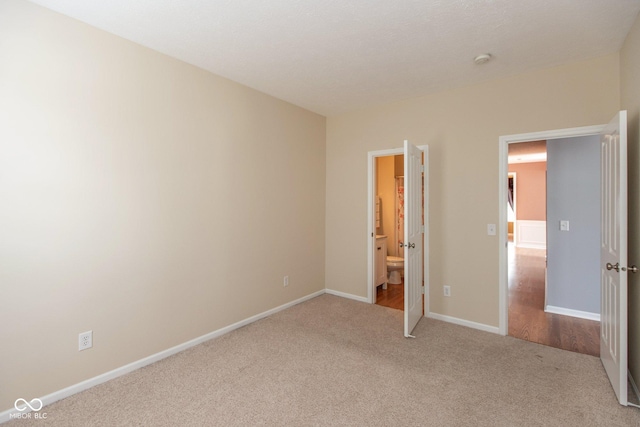 unfurnished bedroom featuring connected bathroom, baseboards, and carpet flooring