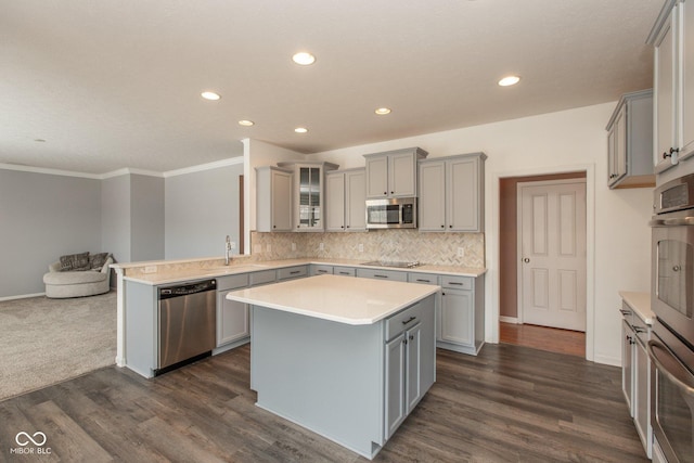 kitchen with a peninsula, a sink, appliances with stainless steel finishes, gray cabinets, and tasteful backsplash