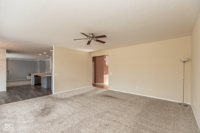 unfurnished living room featuring carpet, baseboards, ceiling fan, and a sink