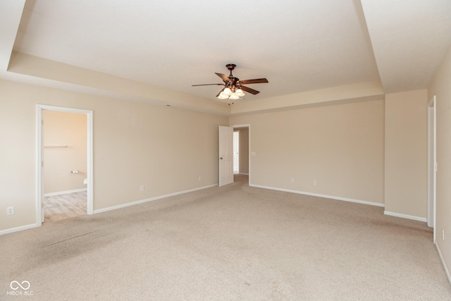 spare room featuring a ceiling fan, a tray ceiling, light colored carpet, and baseboards