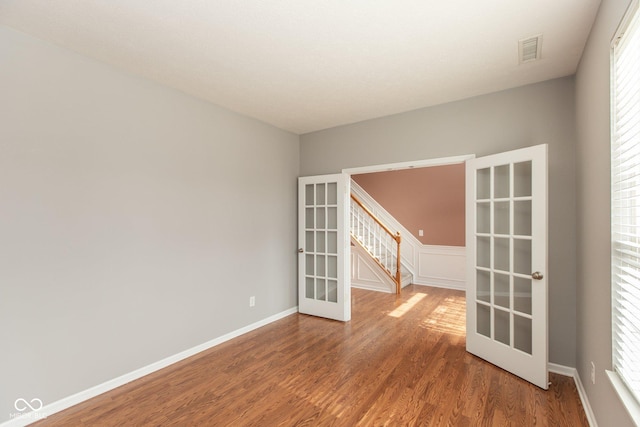 empty room with french doors, wood finished floors, visible vents, and baseboards