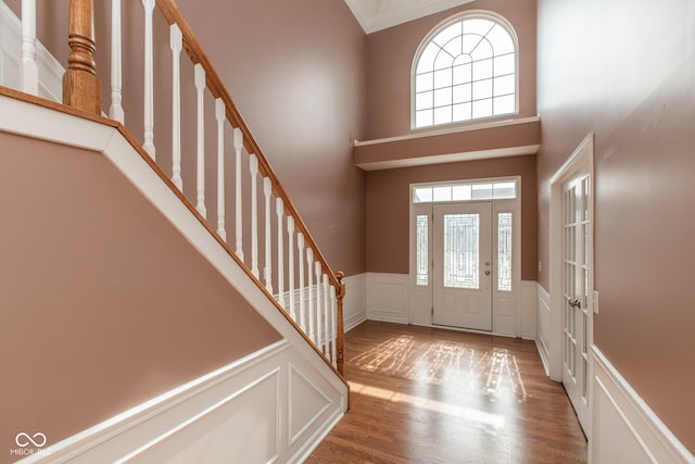 foyer entrance with a wainscoted wall, a decorative wall, stairway, a towering ceiling, and wood finished floors