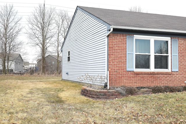 view of home's exterior featuring roof with shingles, brick siding, and a lawn