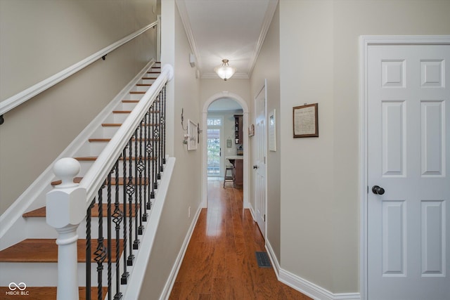 hall with arched walkways, wood finished floors, visible vents, baseboards, and crown molding