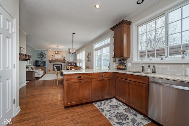 kitchen with ornamental molding, wood finished floors, a peninsula, a brick fireplace, and stainless steel dishwasher