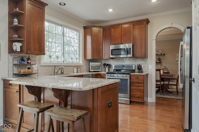 kitchen with stainless steel appliances, a peninsula, a sink, light wood-style floors, and crown molding