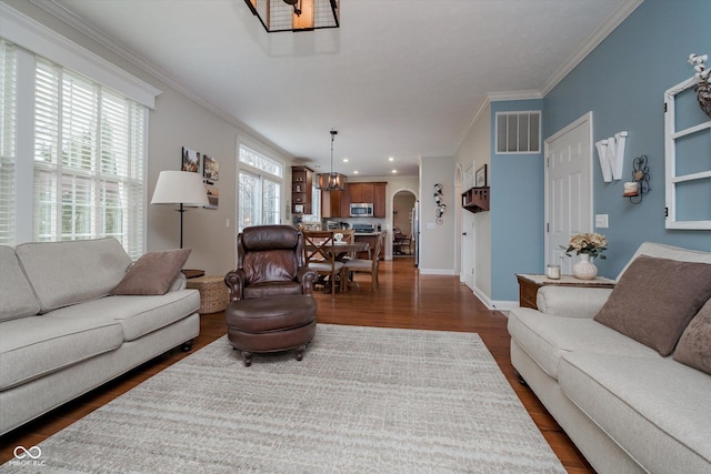 living area with baseboards, visible vents, arched walkways, ornamental molding, and dark wood-type flooring