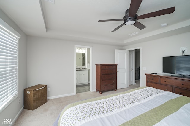 bedroom with visible vents, baseboards, a tray ceiling, light carpet, and ensuite bathroom