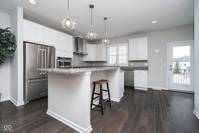 kitchen featuring a kitchen island, decorative backsplash, appliances with stainless steel finishes, wall chimney exhaust hood, and dark wood-style flooring