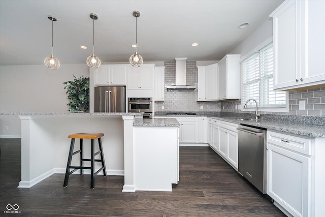 kitchen with a kitchen island, dark wood-style flooring, a sink, stainless steel appliances, and wall chimney range hood