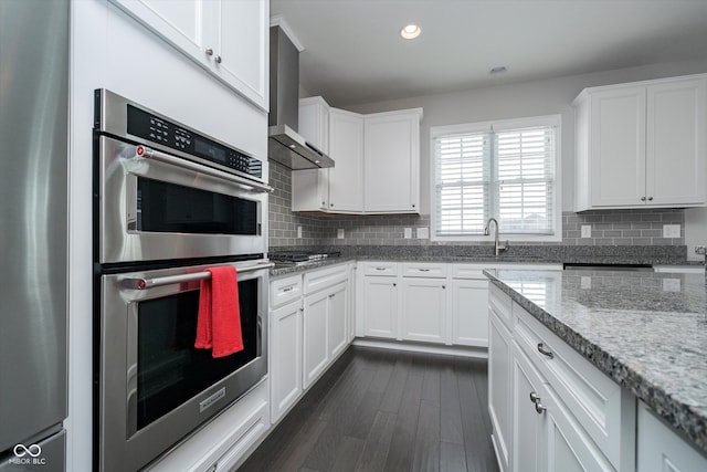 kitchen featuring decorative backsplash, wall chimney range hood, white cabinets, and stainless steel appliances