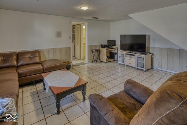 living area with a wainscoted wall, visible vents, a textured ceiling, and light tile patterned flooring