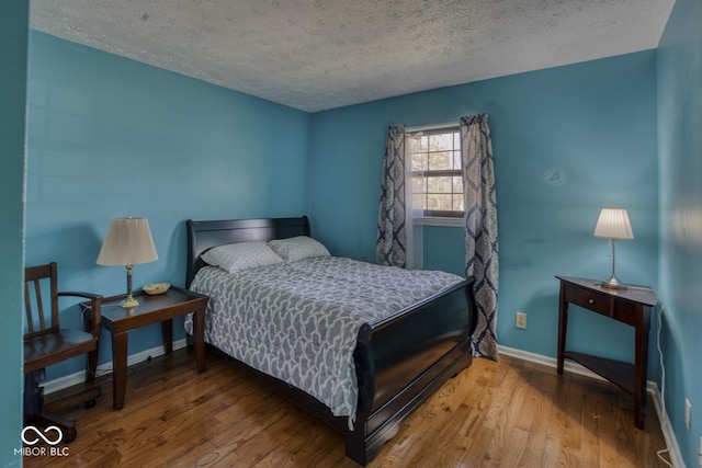 bedroom featuring a textured ceiling, baseboards, and wood finished floors