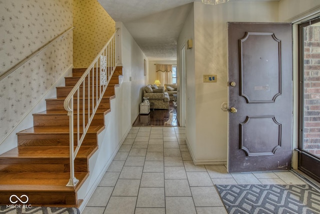 foyer featuring light tile patterned flooring, stairway, baseboards, and wallpapered walls