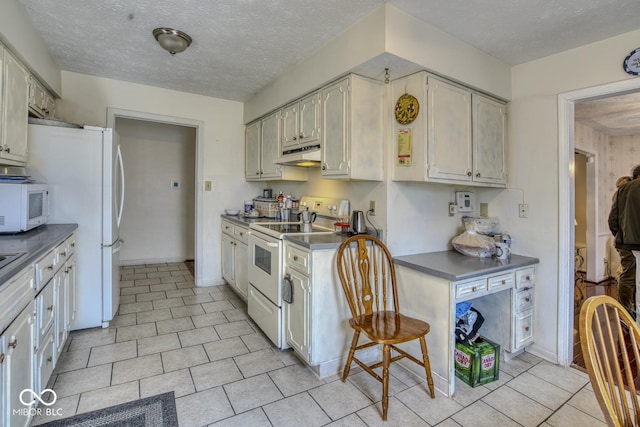 kitchen featuring dark countertops, a textured ceiling, white appliances, under cabinet range hood, and baseboards