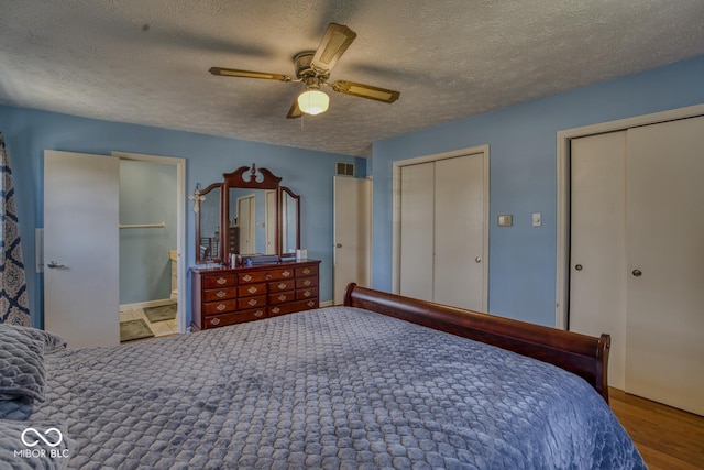 bedroom featuring multiple closets, visible vents, ensuite bathroom, a ceiling fan, and a textured ceiling