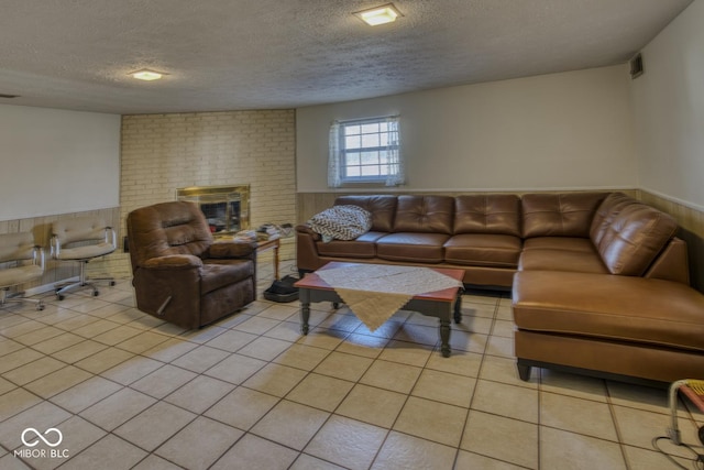 living room with a wainscoted wall, a fireplace, light tile patterned floors, visible vents, and a textured ceiling