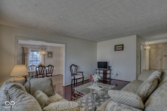 living area featuring a chandelier, a textured ceiling, baseboards, and wood finished floors