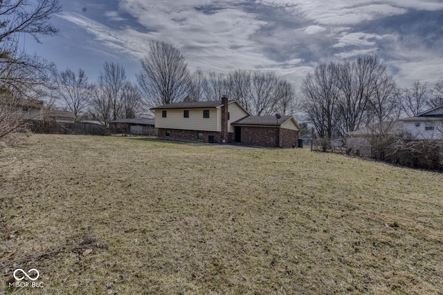 rear view of property featuring brick siding, a lawn, a chimney, and fence