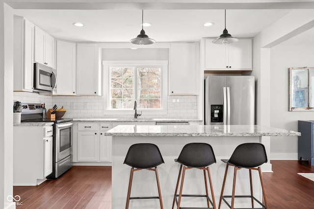 kitchen with a kitchen island, dark wood finished floors, a breakfast bar area, appliances with stainless steel finishes, and white cabinetry