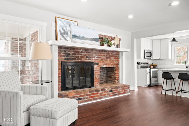 living room with a brick fireplace, recessed lighting, and dark wood-style floors