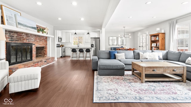 living room featuring recessed lighting, a chandelier, a brick fireplace, and dark wood-style floors