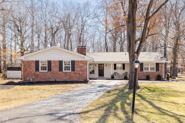 view of front of home featuring a front yard, driveway, covered porch, a chimney, and brick siding