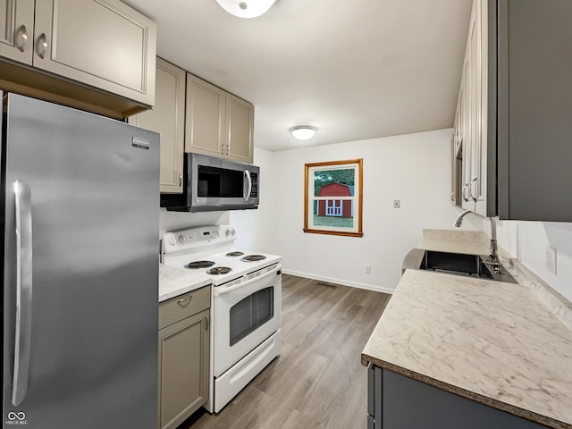 kitchen with stainless steel appliances, wood finished floors, a sink, light countertops, and gray cabinets