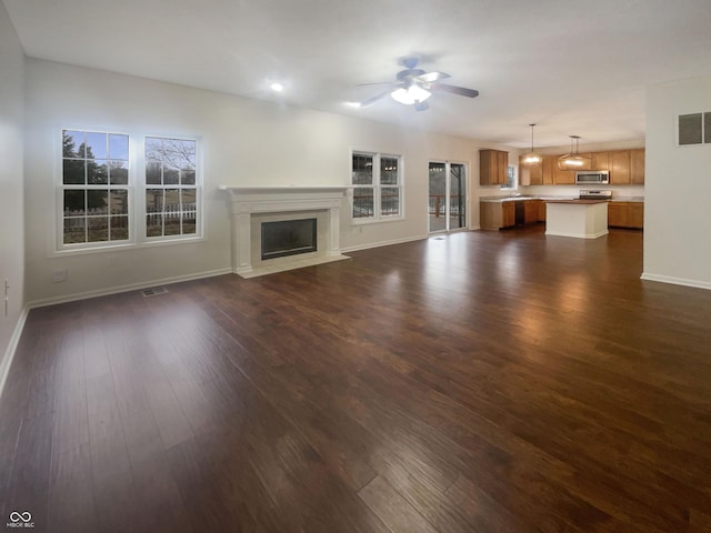 unfurnished living room with a fireplace, visible vents, dark wood-type flooring, a ceiling fan, and baseboards