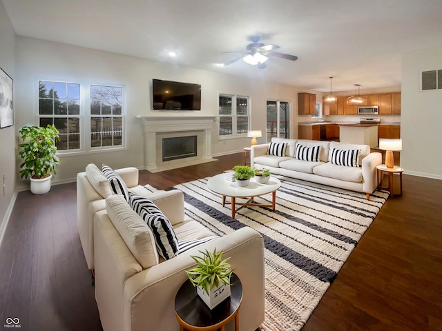 living room with ceiling fan, dark wood-style flooring, a fireplace with flush hearth, visible vents, and baseboards