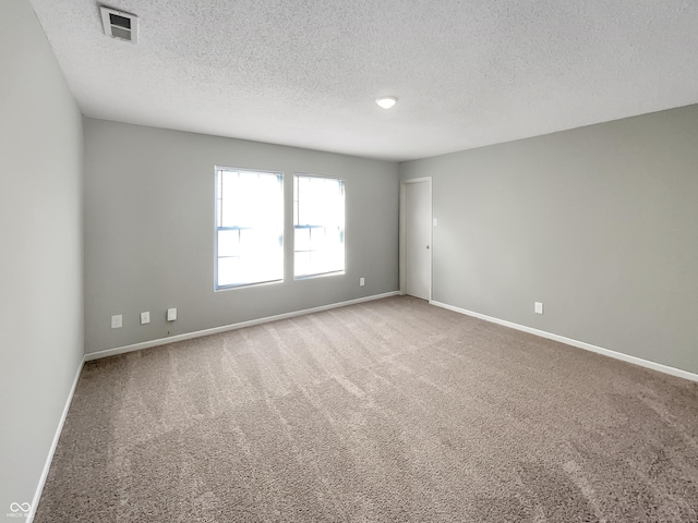 carpeted spare room with baseboards, visible vents, and a textured ceiling