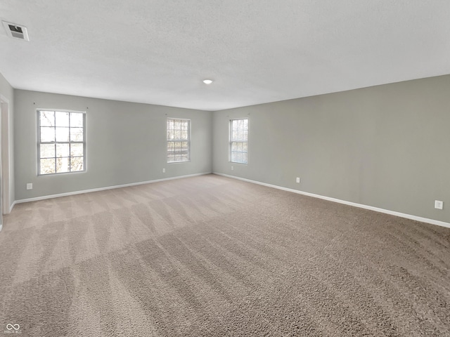 unfurnished room with baseboards, visible vents, a textured ceiling, and light colored carpet