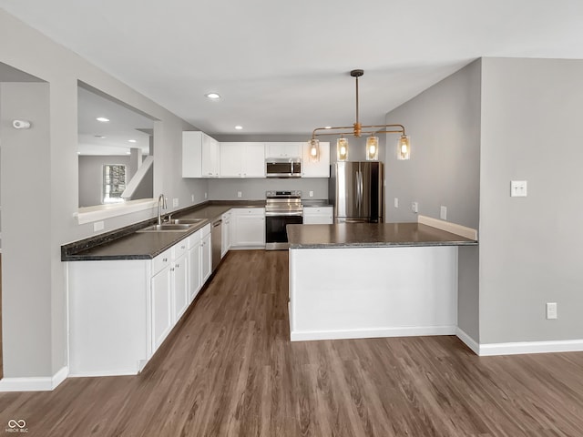 kitchen with a peninsula, dark wood-style flooring, a sink, appliances with stainless steel finishes, and dark countertops