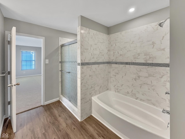 bathroom with a washtub, wood finished floors, a shower with door, and baseboards